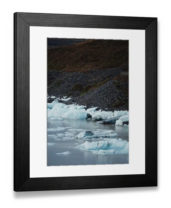 Framed Print : Ice chunks scattered along a rocky shoreline beside still water