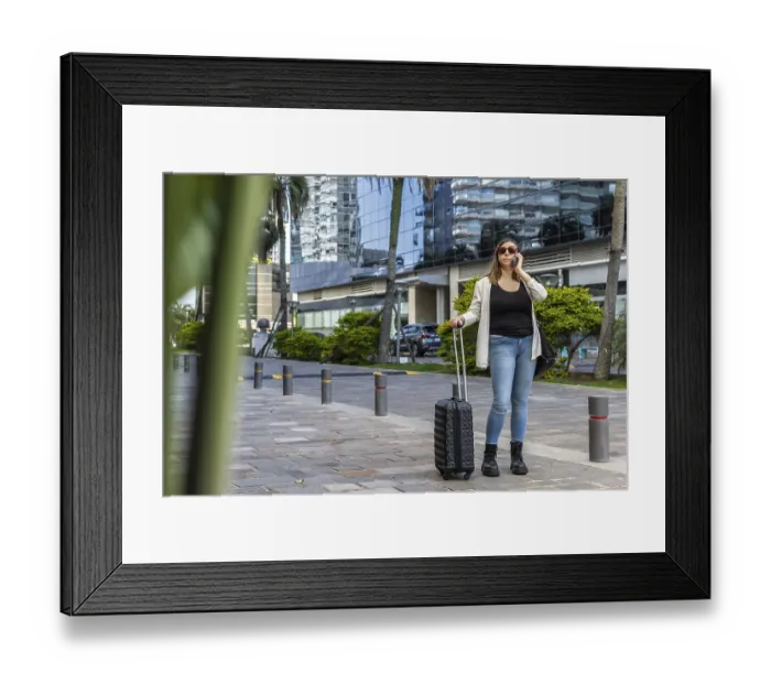 Framed Print : Young businesswoman walks with her suitcase on wheels on a paved street