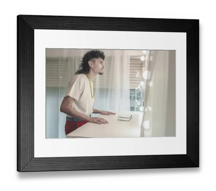 Framed Print : Young man with a mullet hairstyle and a colorful necklace is leaning on a dressing table with glasses on it Framed Print : Young man with a mullet hairstyle and a colorful necklace is leaning on a dressing table with glasses on it