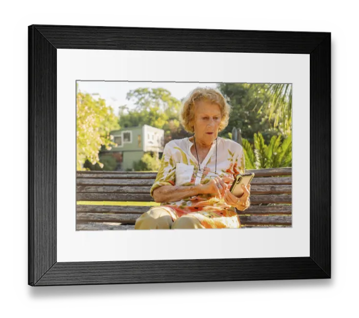 Framed Print : Senior woman sitting on a wooden bench in a sunny park