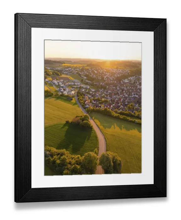 Framed Print : View of a village and a road surrounded by fields and trees at sunset