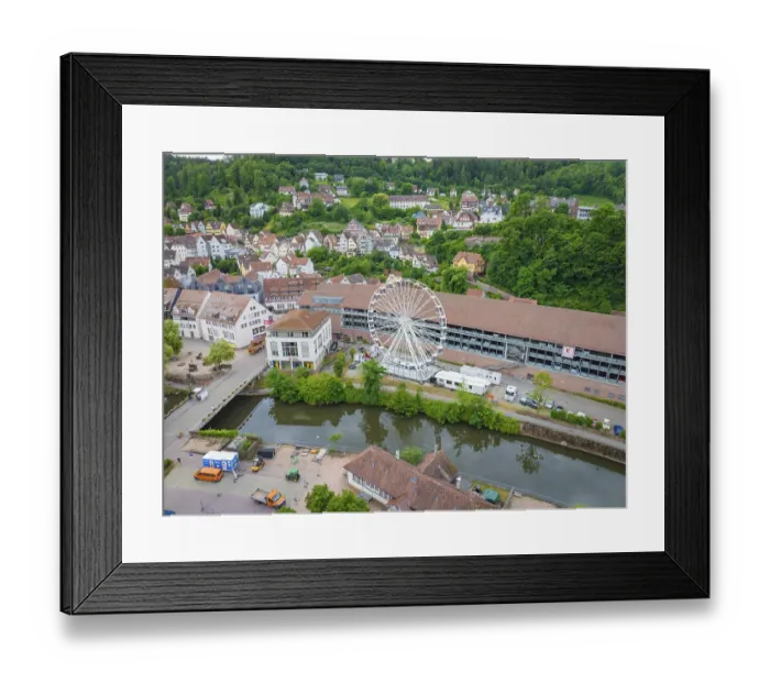 Framed Print : A Ferris wheel next to a river in the centre of a town with a green hilly landscape in the background Framed Print : A Ferris wheel next to a river in the centre of a town with a green hilly landscape in the background