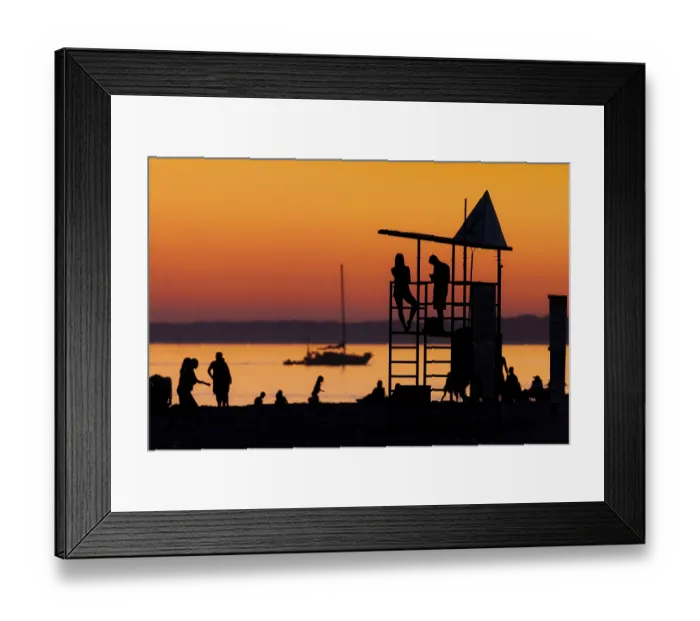 Framed Print : Silhouetted figures against an orange sunset on the beach with a lifeguard tower
