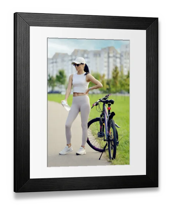 Framed Print : A woman in athletic wear stands on a path in a green park next to her bike