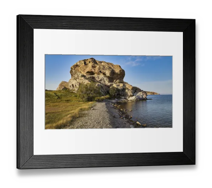 Framed Print : Large rock formation on the coast with clear sky and grassy areas in the foreground