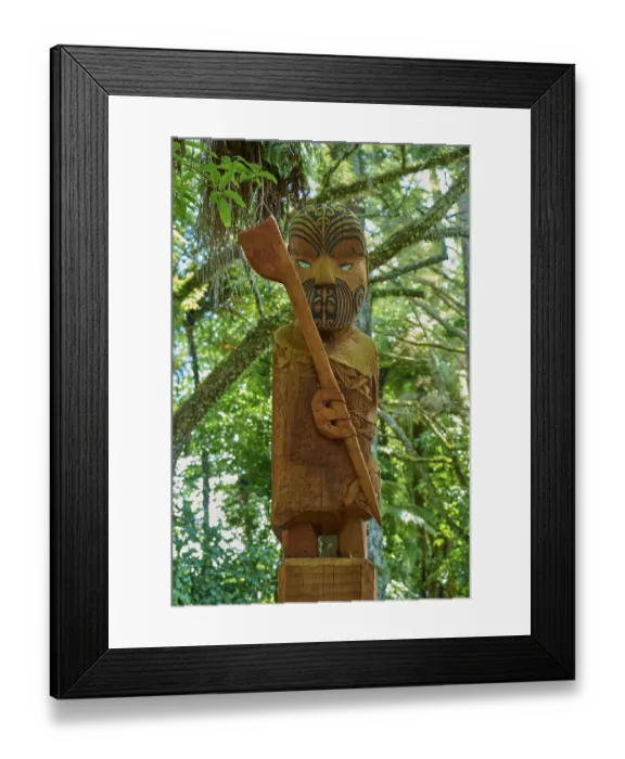 Framed Print : Wooden statue of a Maori with a carved face and head in a lush forest setting