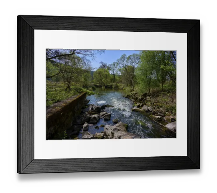 Framed Print : A tranquil river landscape with green trees and stones lining the banks