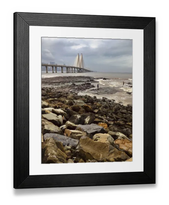 Framed Print : Rocks by the sea with a large bridge and urban background on a cloudy day Framed Print : Rocks by the sea with a large bridge and urban background on a cloudy day