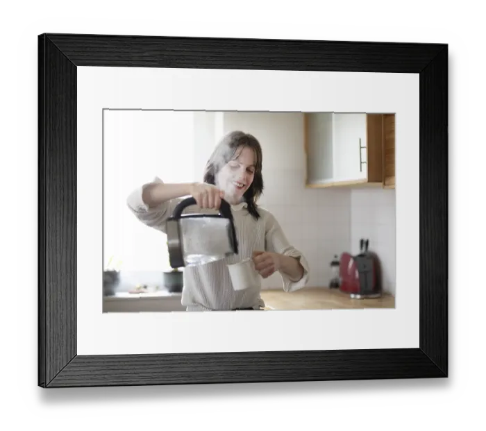 Framed Print : Woman smiles while pouring water into a cup with a kettle Framed Print : Woman smiles while pouring water into a cup with a kettle