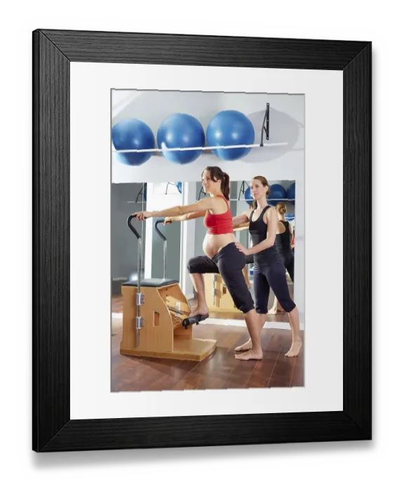 Framed Print : Pregnant woman pilates exercise wunda chair at gym with personal trainer