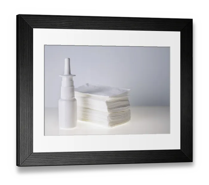 Framed Print : Nasal drops in a white bottle and a stack of handkerchiefs on a white background
