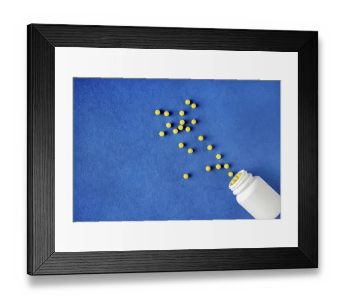 Framed Print : Round yellow vitamins spilled out of a white jar on a blue background