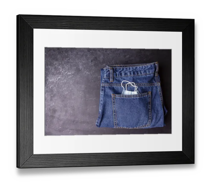 Framed Print : A medical mask peeks out from a jeans pocket on a black background