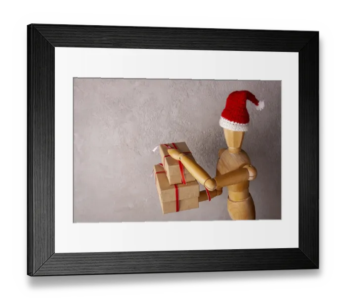 Framed Print : Wooden man in a santa hat holds a gift in a red box copy space Framed Print : Wooden man in a santa hat holds a gift in a red box copy space