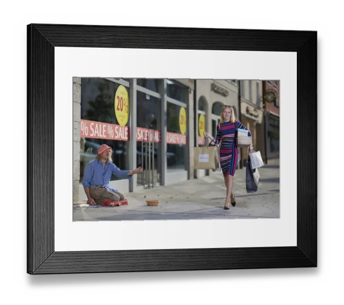 Framed Print : Woman with shopping bags walks past a homeless man on the street