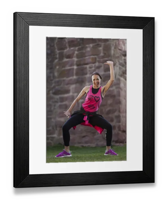 Framed Print : Smiling woman in sportswear in dynamic Zumba pose in front of a stone wall