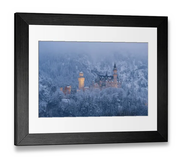 Framed Print : The castle is illuminated and lies in the middle of a snow-covered forest and foggy mountains