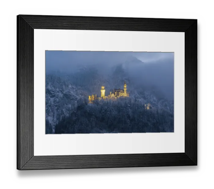 Framed Print : Illuminated castle surrounded by snow-covered mountains in a gloomy atmosphere