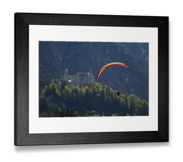 Framed Print : A paraglider glides over Neuschwanstein Castle against a mountainous backdrop Framed Print : A paraglider glides over Neuschwanstein Castle against a mountainous backdrop