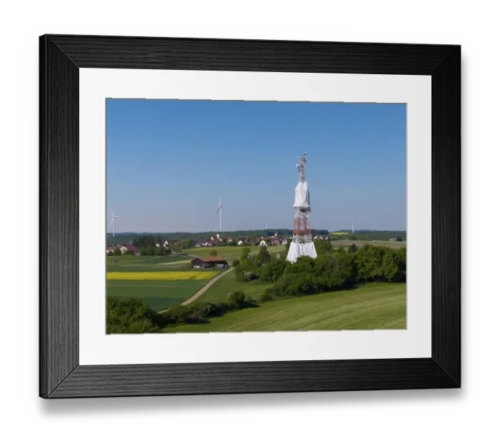 Framed Print : A transmission tower and wind turbines near a village under a blue sky