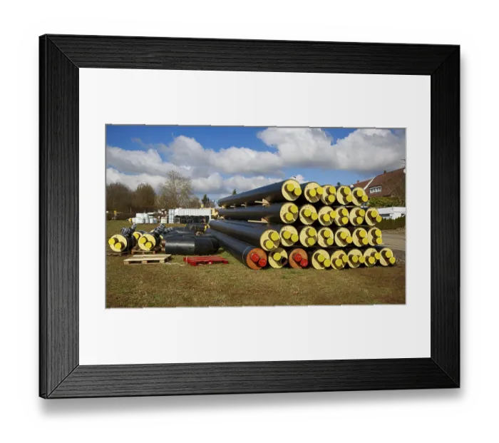 Framed Print : Stacked district heating pipes and district heating lines with yellow ends lie piled up in a meadow