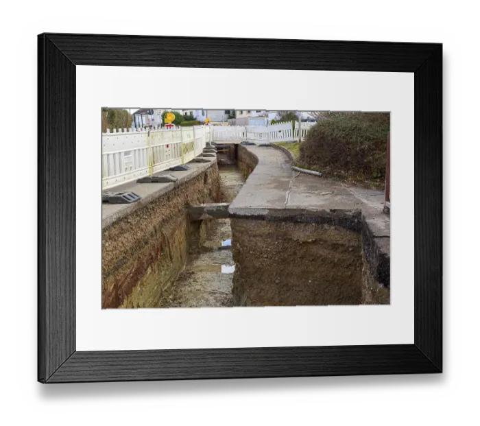 Framed Print : Deep road trench with construction barriers and earthworks in progress