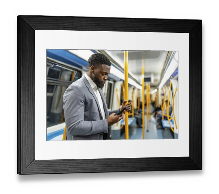 Framed Print : Young businessman using a smartphone while standing on a subway train during his daily commute through the bustling