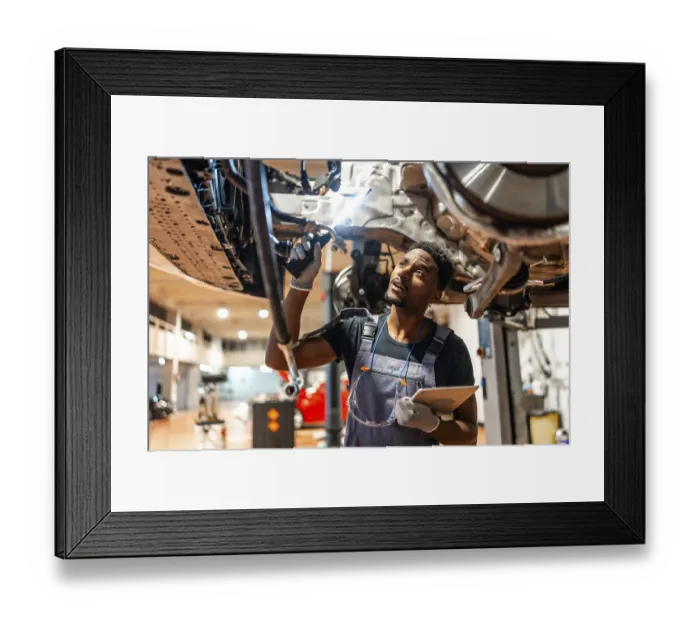Framed Print : Young mechanic inspecting car chassis using flashlight and holding tablet in a modern workshop