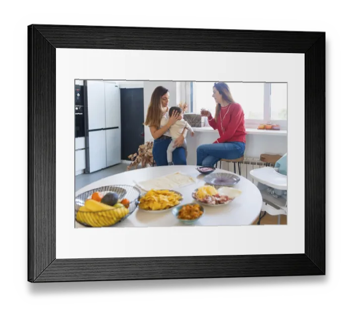 Framed Print : Two mothers are chatting and drinking juice in a modern kitchen