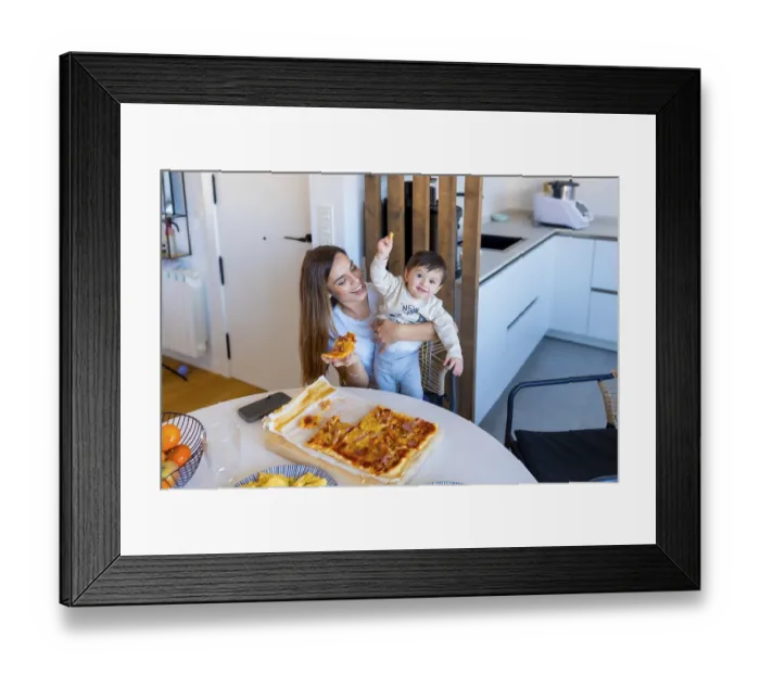 Framed Print : Happy mother holding her baby while eating pizza in a bright
