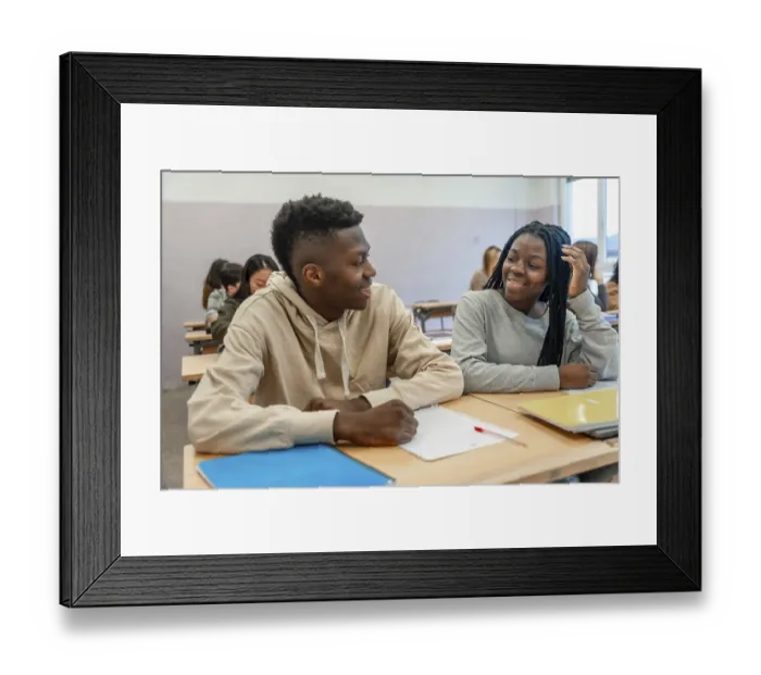 Framed Print : Two college students smiling and engaging in conversation during a lesson Framed Print : Two college students smiling and engaging in conversation during a lesson