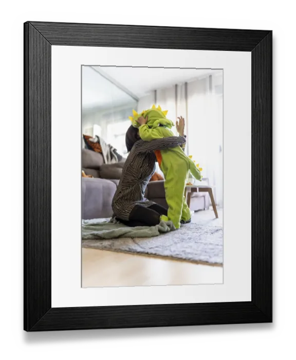 Framed Print : Mother kneeling on carpet and hugging her son wearing a dinosaur costume while playing together in the living room