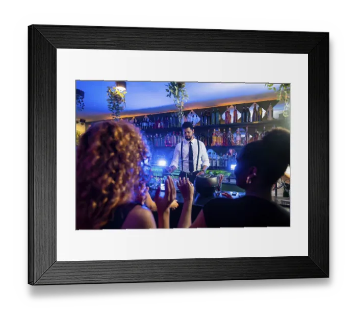 Framed Print : Young bartender preparing cocktails for cheering customers in a trendy bar with blue lights and hanging plants