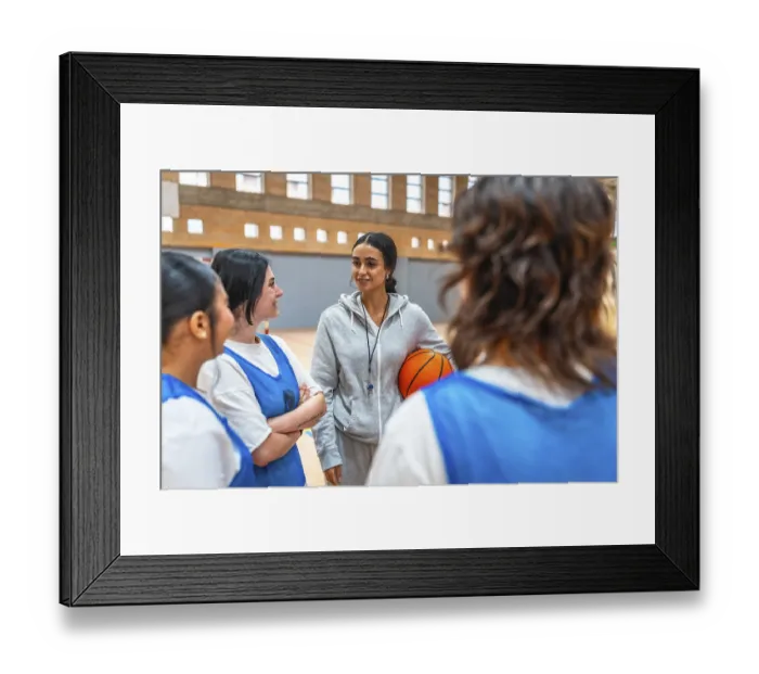Framed Print : Female basketball coach holding a ball and engaging with her team during an intense training session in the gym Framed Print : Female basketball coach holding a ball and engaging with her team during an intense training session in the gym