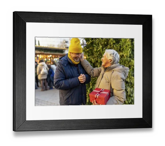 Framed Print : Loving senior couple exchanging christmas gifts at a traditional christmas market Framed Print : Loving senior couple exchanging christmas gifts at a traditional christmas market
