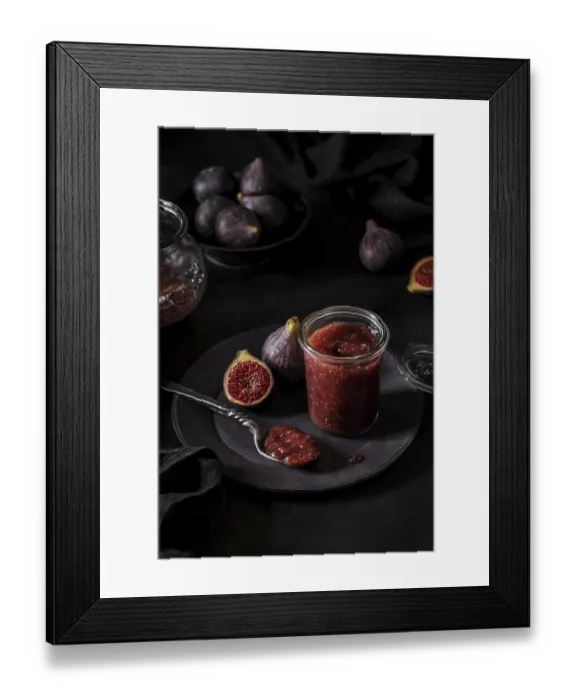 Framed Print : From above fresh fruit jam in small jar and on spoon with full and cut figs on plate at black kitchen table