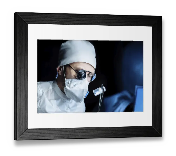 Framed Print : A masked and capped surgeon in glasses focuses intently against a dark background