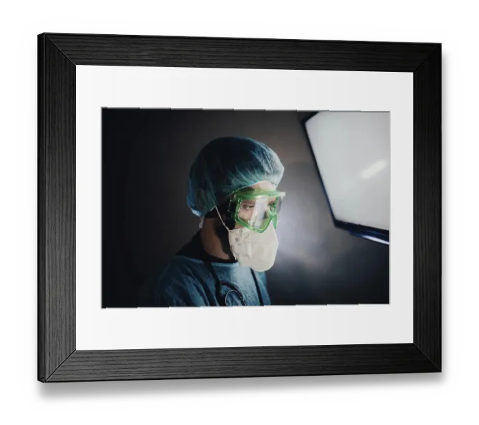 Framed Print : A focused medical professional in protective gear looking at a screen