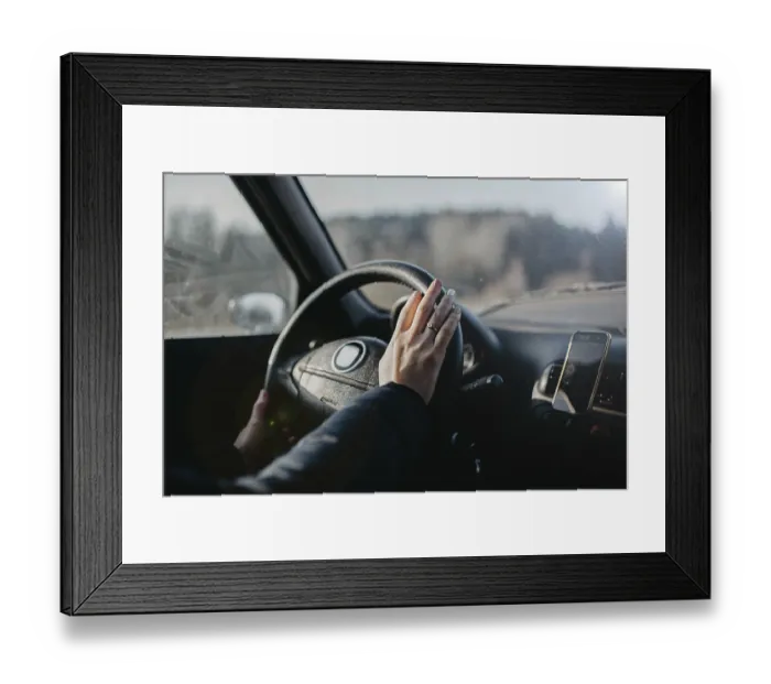 Framed Print : A hand on the steering wheel inside a car with a smartphone holder attached