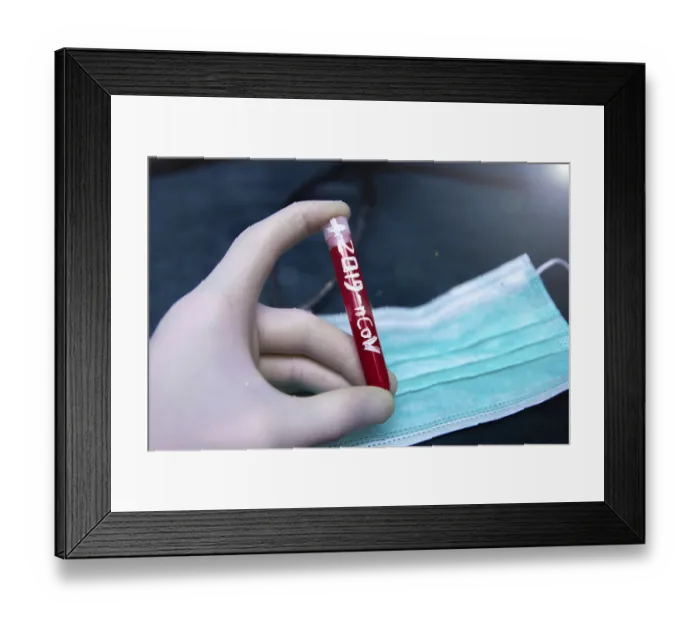 Framed Print : A hand holding a test tube labeled 2019-nCoV over a medical mask