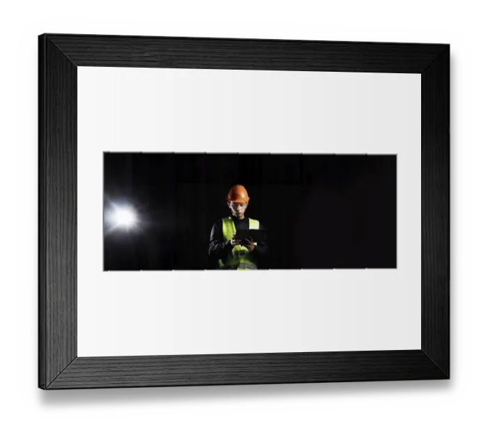 Framed Print : A construction worker in safety gear uses a tablet under spotlight against a dark backdrop