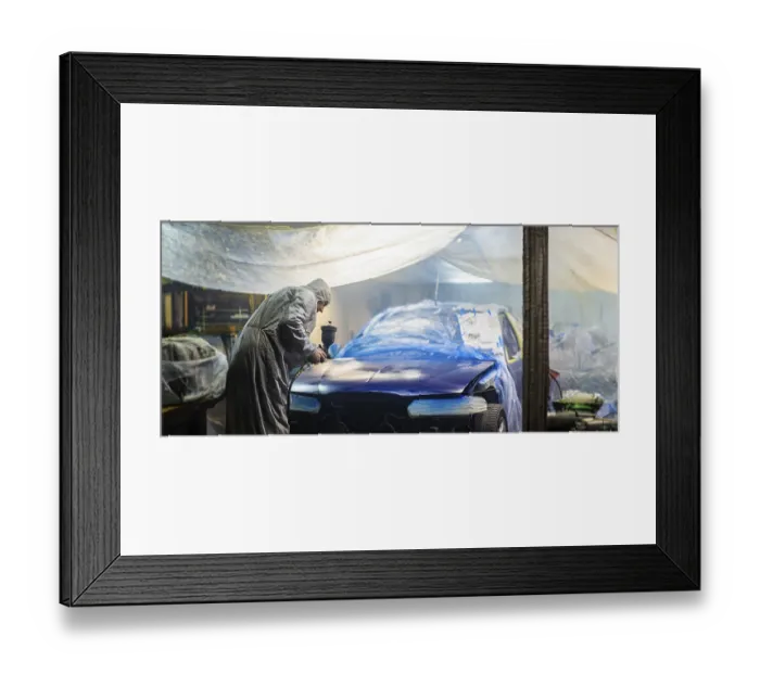 Framed Print : Person in protective suit spray painting a car in a dimly lit garage