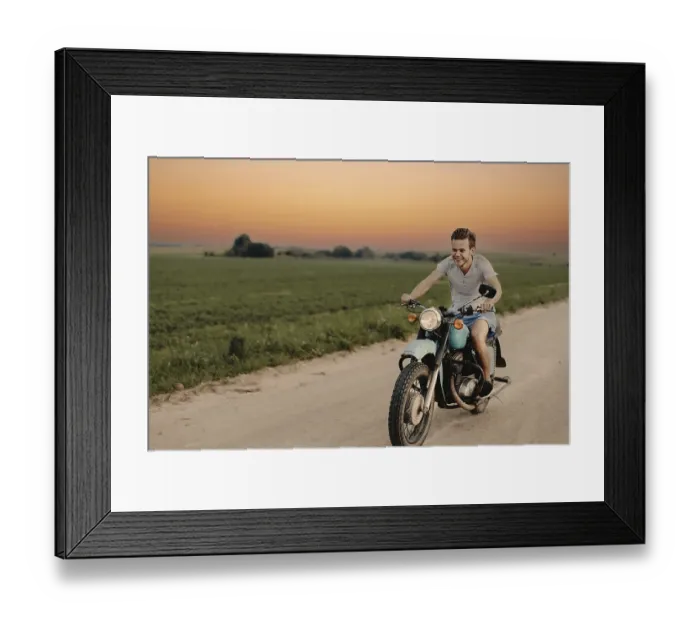Framed Print : A smiling man rides a motorcycle down a rural road at sunset