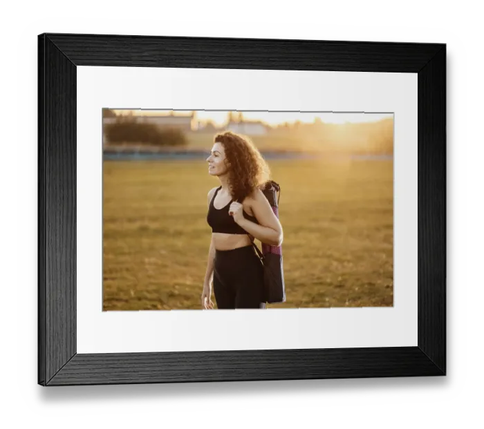 Framed Print : A woman stands in a field with a yoga mat over her shoulder at sunset