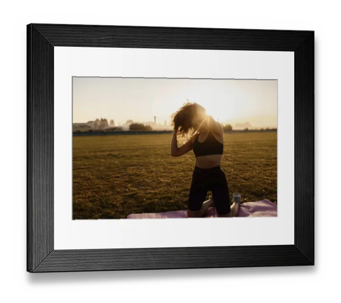 Framed Print : Woman adjusting hair while kneeling on a yoga mat in the sunlight