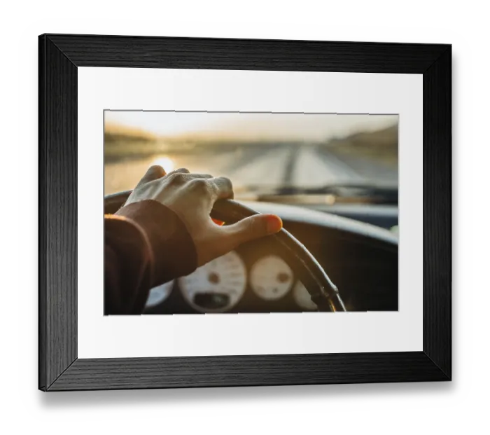 Framed Print : A hand on the steering wheel driving down a highway during a sunset
