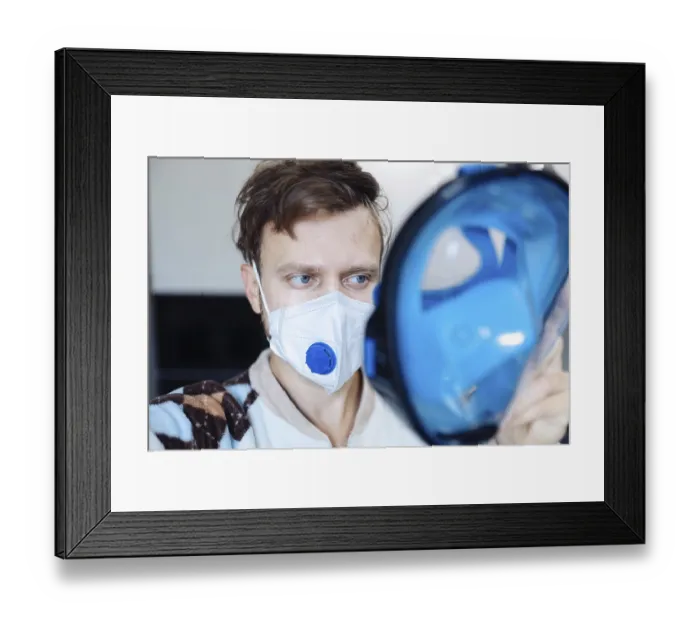 Framed Print : A person wearing a mask, holding a blue face shield