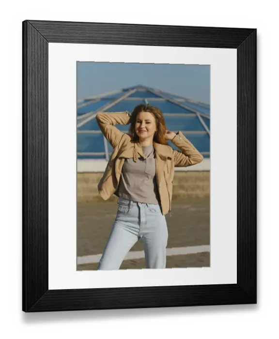 Framed Print : Young woman poses confidently in casual outfit against modern glass structure on sunny day