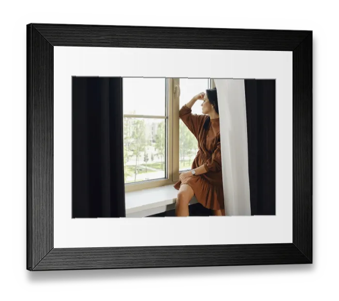 Framed Print : A woman is seated by a window, dressed in a brown dress