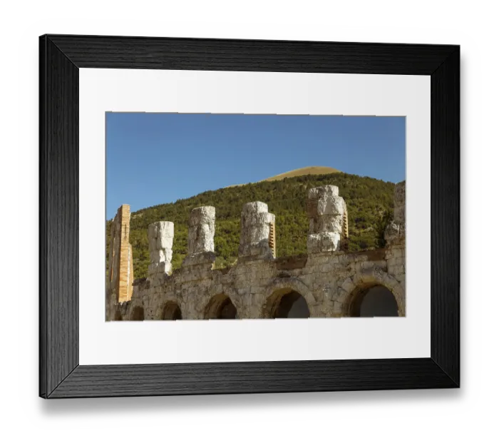 Framed Print : Detail of the ancient Roman theatre in the background the Ingino mountain full of green fir trees